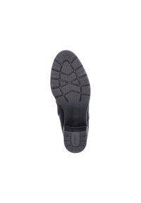 Semelle de chaussure noire en caoutchouc texturé avec une prise, présentant un motif en zigzag et un logo imprimé. Forme arrondie avec un design de talon robuste.