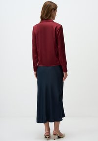 Crimson satin blouse paired with a flowing navy blue skirt, featuring a smooth texture and a fitted silhouette, with back-button details.