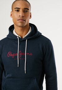 Navyblauwe katoenen hoodie met een rode geborduurde "Pepe Jeans London" logo, witte trekkoorden en een voorzak. Zachte textuur.