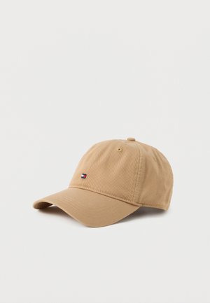 Gorra de béisbol beige con visera curva y pequeño logotipo rectangular en rojo, blanco y azul marino en la parte frontal, presentada sobre un fondo blanco liso.