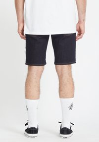 Donkerdenim shorts met een rechte snit, contrasterende oranje stiksels, gedragen met witte crew-sokken en zwarte sneakers met logo.