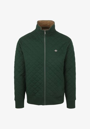 Gesteppte grüne Jacke mit Reißverschluss und Stehkragen, mit einem kontrastierenden braunen Cordfutter und einem kleinen Logo auf der Brust.