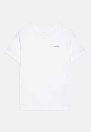 Balta īsroku t-krekls ar apaļu kakla izgriezumu un mazu melnu "Calvin Klein" logotipu kreisajā krūtīs, attēlots uz vienkārša fona.