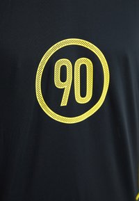 Čierne atletické tričko s výraznou žltou grafikou čísla "90" v žltom kruhovom obryse. Materiál je hladký a priedušný.