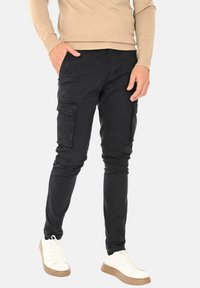 Pantaloni cargo neri con vestibilità slim, dotati di tasche laterali e realizzati in un morbido cotone. Abbinati a scarpe da ginnastica bianche e un maglione beige.
