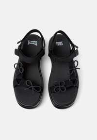 Sorte sandaler med polstret såle, justerbare stropper og dekorative sløyfeakenter. Har logoene "CAMPE" og "TWINS" på innersålene.