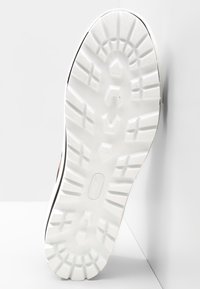 Biała podeszwa sneakerów z głębokimi wzorami bieżnika, wykonana z gumowego materiału, z lekkim występem na pięcie. Czysty design z teksturowanymi akcentami.