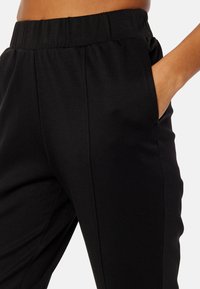 Zwarte broek van een zachte, gestructureerde stof, met een elastische tailleband en zijzakken. Het ontwerp is losvallend met een gladde afwerking.