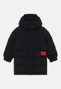 Doudoune noire avec un col haut, deux poches avant et une étiquette rouge vif comportant "HUGO". Design texturé et isolé.