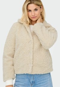 Cream-colored fleece jacket with a textured, fluffy surface, button closure, and a hood; features ribbed cuffs and a relaxed fit.