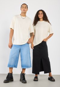 Beige oversized t-skjorte, blå vide denimshorts, svart maxiskjørt med frontslitt, svarte snøresko, og svarte sandaler.