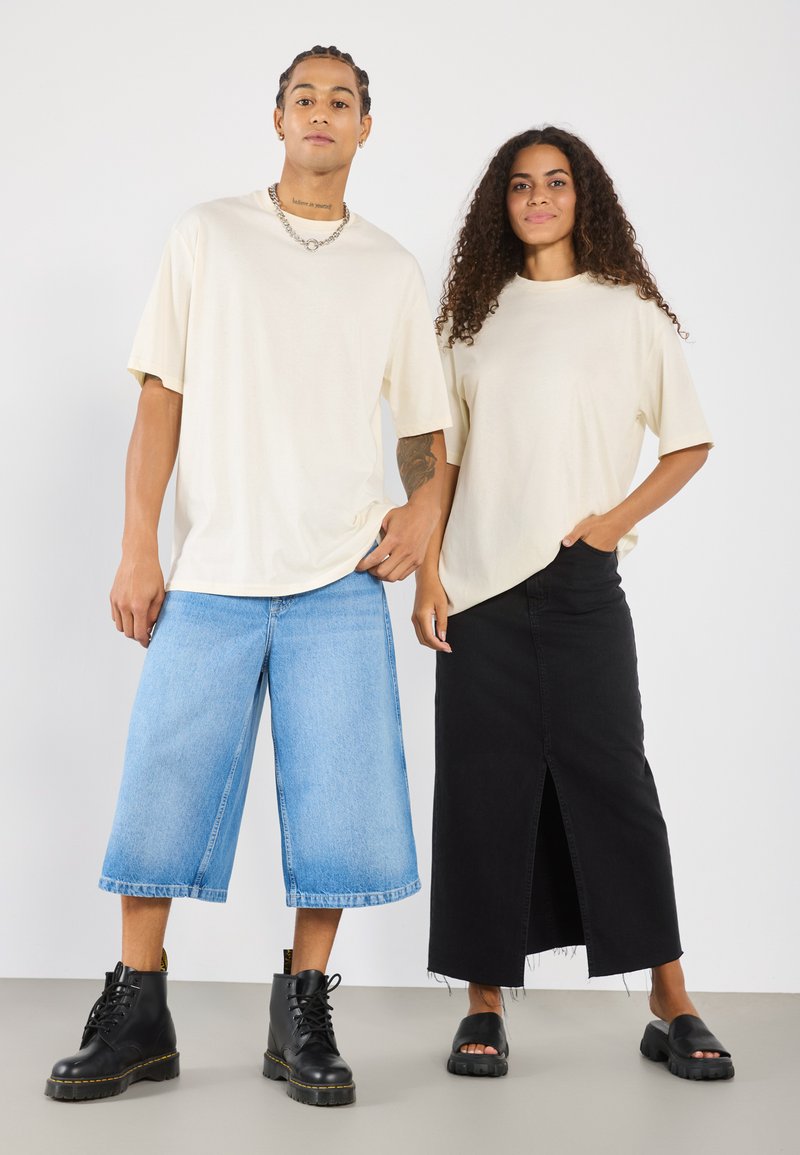 Beige oversized t-skjorte, blå vide denimshorts, svart maxiskjørt med frontslitt, svarte snøresko, og svarte sandaler.