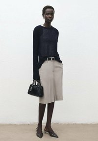 Pulover tricotat bleumarin, fustă bej până la genunchi, geantă neagră, tocuri negre ascuțite și un băț argintiu. Texturi netede, design minimalist.