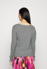 Pull en tricot gris avec des manches longues et un col bateau, porté sur une jupe plissée multicolore ornée de motifs floraux.