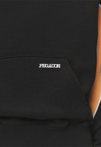 Černá mikina s kapucí a přední kapsou, která má vyšívané bílé logo "PEGADOR". Texturovaná, měkká tkanina s oranžovými postranními akcenty.