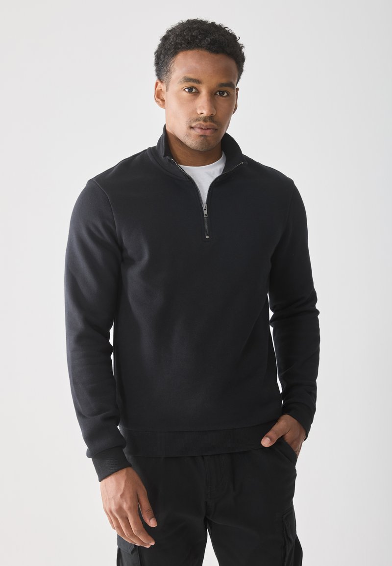 Zwarte sweatshirt met rits en hoge kraag, lange mouwen en ribgebreide manchetten. Draag het over een wit shirt, met een gladde, zachte textuur.