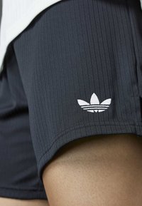 Black ribbed athletic shorts made of fabric with a white Adidas logo on the hem. The design features a fitted style and smooth texture.