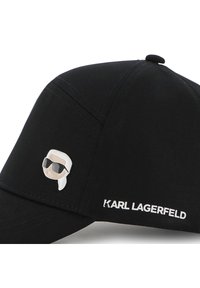 Μαύρο καπέλο από βαμβάκι με λευκό λογότυπο και σμάλτο καρφίτσα με στυλιζαρισμένο πρόσωπο με γυαλιά ηλίου στο μπροστινό αριστερό μέρος.