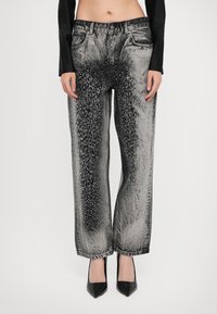 Woman wearing high-waisted wide-leg jeans with a black and silver metallic gradient and rhinestone pattern, paired with black pointed heels.