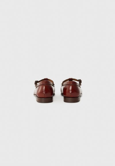 Chaussures en cuir rouge foncé avec une finition lisse, bout arrondi et brides ajustables au niveau des talons, reposant sur une semelle marron.