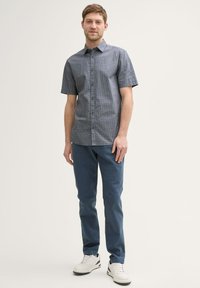 Korte mouwen overhemd met knopen in donkerblauw met een geometrisch patroon, gecombineerd met lichtblauwe broek en witte sneakers. Gladde stoftextuur.