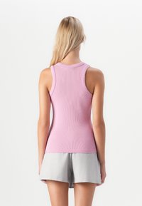 Woman with long blonde hair wearing a sleeveless pink ribbed top and light gray shorts, shown from the back against a plain white background.
