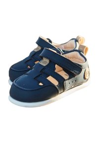 Zapatos infantiles de color azul marino con parte superior texturizada, diseño de punta cerrada, cinta de velcro y suela de goma blanca. Un detalle circular como acento en el lateral.