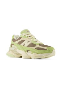 Baskets épaisses en daim vert clair, panneaux en mesh beige, lacets blancs et semelle épaisse crème, inclinées vers la droite sur fond blanc.