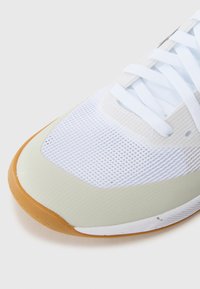 Sneaker med en hvid mesh-overdel, lysegrønne accenter og sål af gummigummi. Inkluderer hvide snørebånd og teksturerede detaljer langs siderne.
