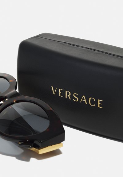 Ochelari de soare din scoică, cu lentile întunecate, având o ramă chunky și accente aurii. Însoțiți de un toc negru cu inscripția "VERSACE" în litere aurii.