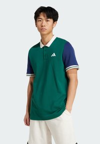 Green polo shirt featuring a white collar and blue sleeves with white and green stripes. Includes a small white logo on the chest.