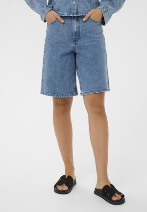 Denim shorts in een lichte blauwe wassing met een rechte pasvorm, voorzien van voorzakken en een taille tot halverwege de heup. Gecombineerd met zwarte slide sandalen.