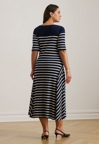 Navy and cream striped maxi dress with short sleeves, flared hem, side slits, and smooth fabric. Worn with black slingback heels.
