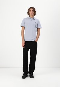 Lys grå polo t-shirt med sorte detaljer, korte ærmer og krave. Sammen med sorte lige bukser og sorte sko.