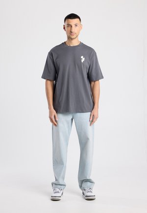 Grijs katoenen t-shirt met korte mouwen en een ronde hals, met een kleine witte afbeelding op de borst, gecombineerd met lichtblauwe jeans en sneakers.