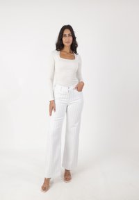 Pantalones de pierna ancha a rayas blancas con cintura alta, combinados con una blusa ajustada de manga larga en color crema. Sandalias de tacón de acrílico transparente completan el look.