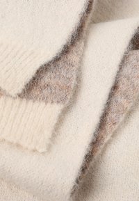 Cremefarvet og taupe tekstureret uldstof med fin pels, der har en blanding af ribbede og glatte mønstre samt lagdelte overlappende sektioner.