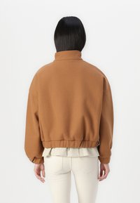 Sweatshirt marron surdimensionné avec un col cheminée, un ourlet côtelé et des manches à poignet. Superposé à une chemise de couleur claire. Texture de tissu lisse.