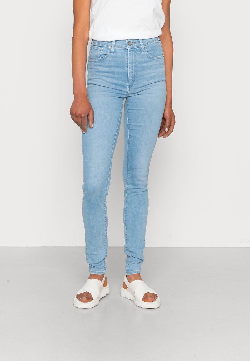 Jeans ajustados de color azul claro fabricados en denim, con una cintura de altura media, bolsillos frontales y una clásica cremallera. Combinados con sandalias blancas.