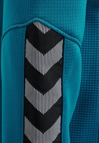 Nærbillede af blåt stof med sort og hvid chevronmønstret stribe og tekstureret syning.