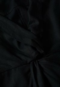 Gros plan sur un tissu noir avec des plis rassemblés et torsadés créant texture et profondeur.