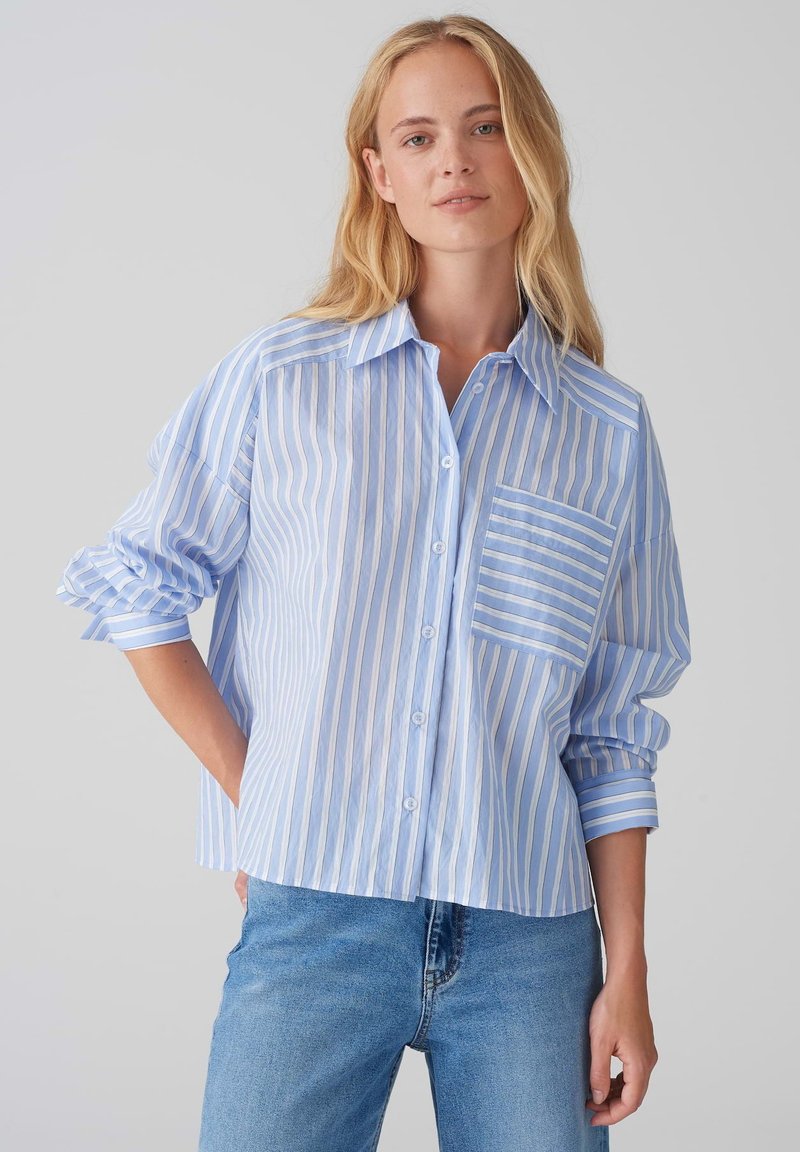 Camicia azzurra a righe con un'unica tasca sul petto, vestibilità comoda e maniche arrotolate, abbinata a jeans in denim blu chiaro.
