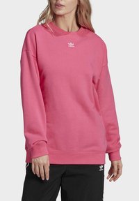 Růžová bavlněná mikina s kulatým výstřihem a dlouhými rukávy. Na prsou má malý bílý logo Adidas a žebrované manžety.