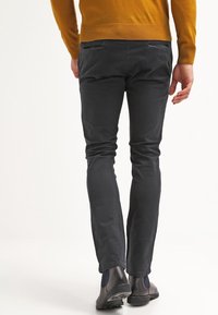 Chinos slim-fit gris foncé avec poches arrière, associés à un pull moutarde et des bottines grises, présentant une texture douce et mate.