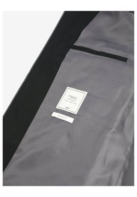 Indersiden af sort jakke, gråt foer med et diskret mønster. Mærkerne viser "next," "40R" og "slim fit." Har en lomme og en glat tekstur.