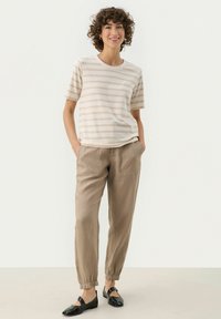 Striped beige cotton t-shirt with short sleeves, paired with light brown linen trousers featuring an elasticated waistband and side pockets.