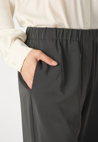 Hlače z elastičnim pasom v temno sivi barvi, z bočnimi žepi. Narejene iz gladkega materiala, sproščenega kroja s subtilnimi gubami.