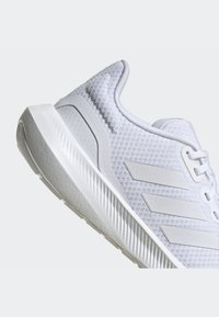 White athletic shoe with a textured mesh upper, flat laces, three side stripes, and a cushioned outsole.