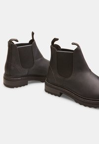 Botas Chelsea negras de cuero con paneles laterales elásticos, tiradores y suelas texturizadas. Presentan un grueso pespunte de contraste y una punta redondeada.