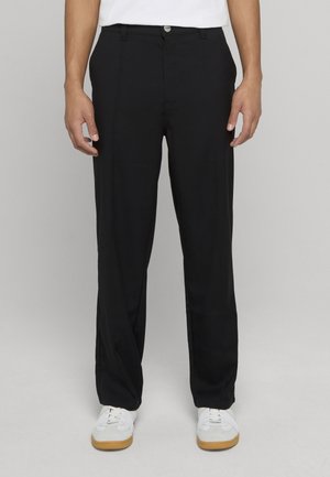 Svarta byxor med smal passform, slätt tyg, framvik och knappstängning, kombinerade med vita sneakers och en enfärgad skjorta.